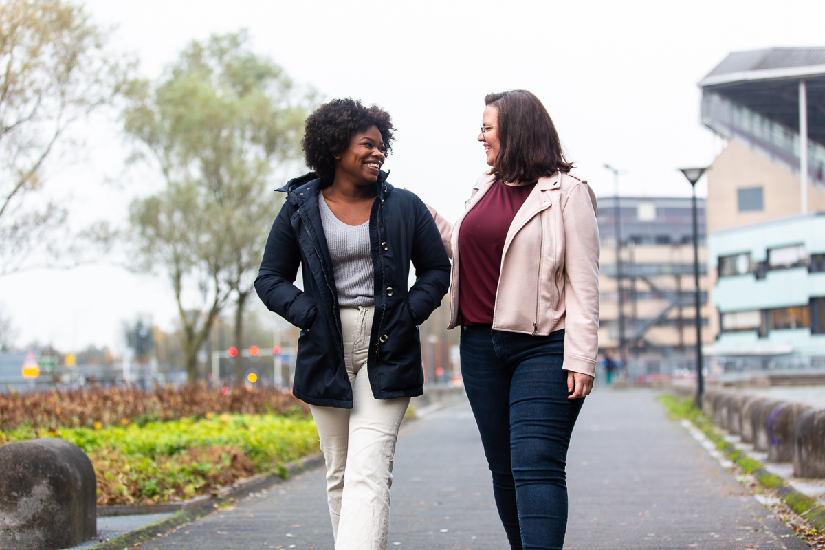 Twee vrouwen lopen buiten en lachen naar elkaar